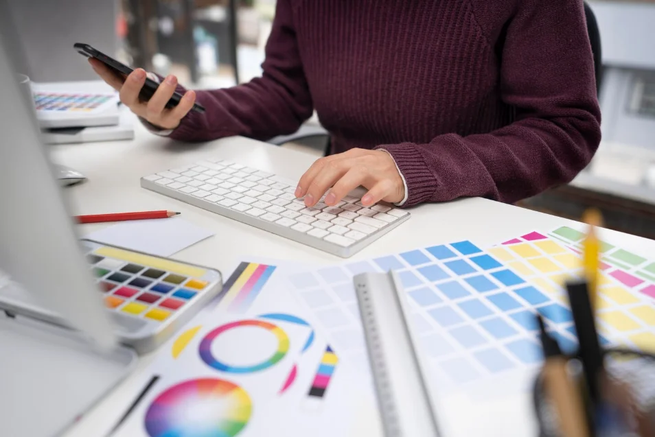 Diseñadora trabajando en su computadora mientras revisa muestras de colores para un proyecto creativo, una parte fundamental del proceso en agencias creativas en España