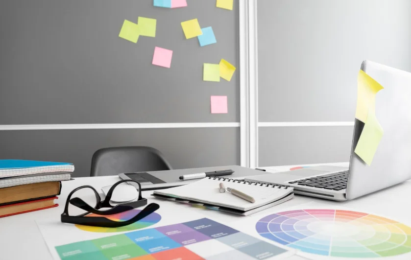 Escritorio de diseño con ordenador, paletas cromáticas y notas adhesivas, típico entorno de los mejores estudios creativos en España