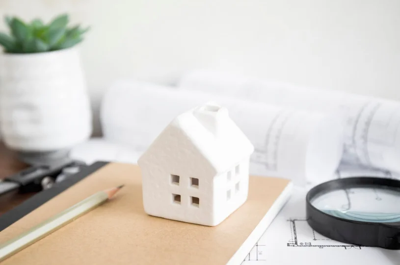 Maqueta de casa blanca sobre planos inmobiliarios con lupa y lápiz, concepto de valoración y compra de vivienda en las mejores inmobiliarias en Valencia