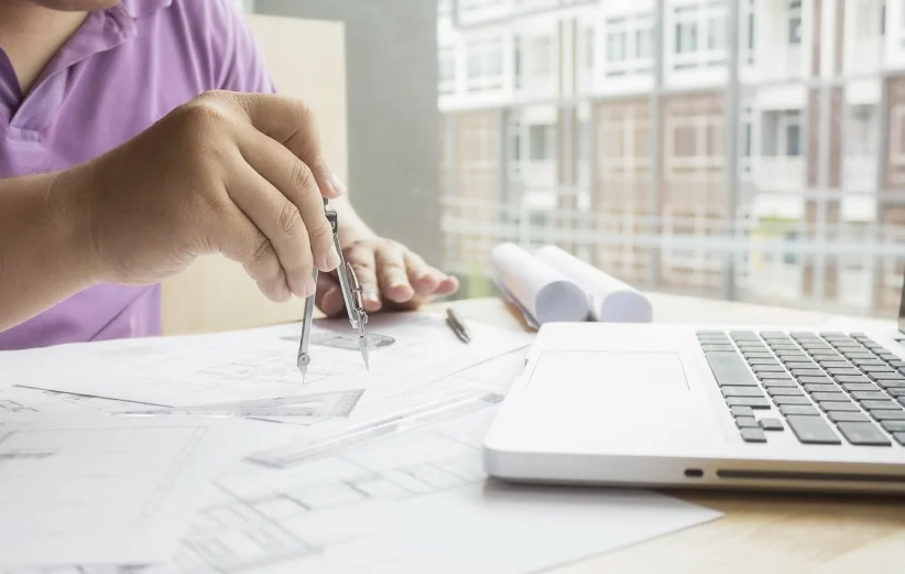 Arquitecto trabajando con planos y compás junto a portátil en mesa de diseño en uno de los mejores estudios de arquitectura en Madrid