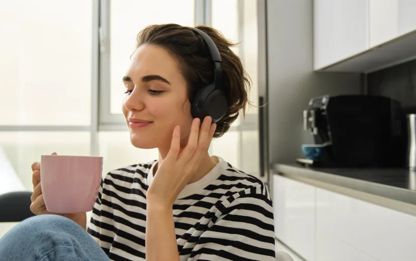 Mujer escuchando un podcast desarrollo personal con auriculares mientras toma una taza de café en casa