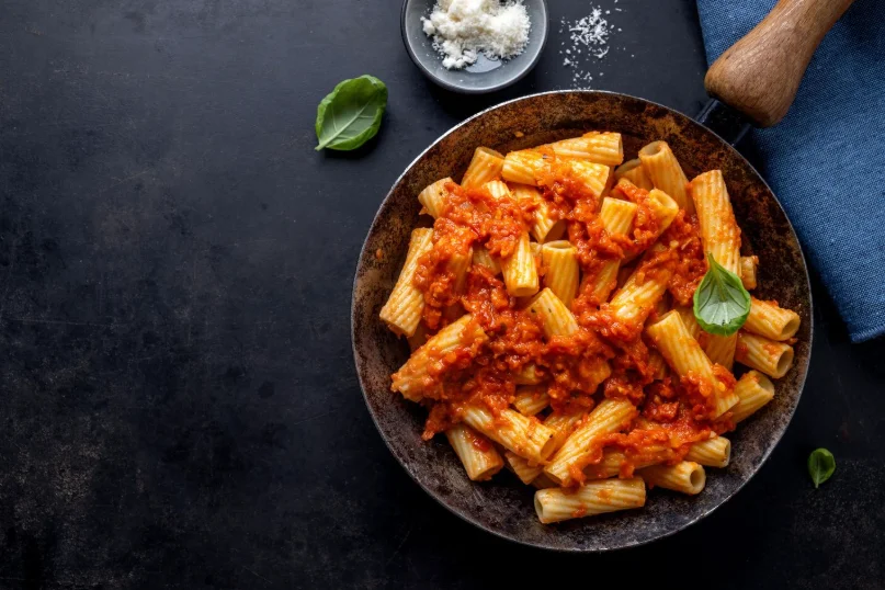 Pasta rigatoni con salsa de tomate servida en un plato oscuro sobre fondo negro