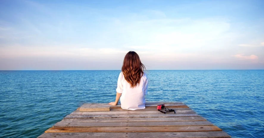 Mujer sentada en un muelle frente al mar en actitud tranquila y reflexiva